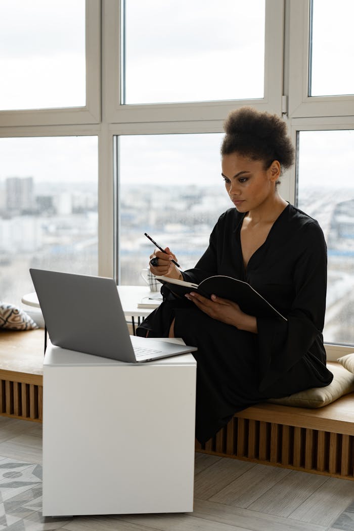 A Woman Writing in Notebook Looking the laptop